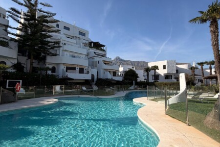 Communal swimming pool at Coto Real I on Marbella’s Golden Mile, surrounded by elegant white Andalusian-style residences, palm trees and landscaped gardens, with La Concha Mountain rising in the background under clear blue skies.